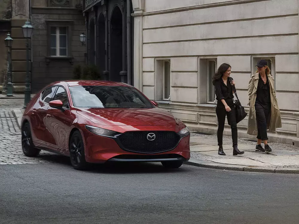 Red Mazda3 Sport driving past pedestrians in a historic district